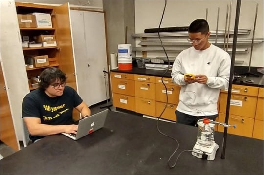 Two Everett Community College students using a Fluke 52 II Dual Probe Digital Thermometer to measure the temperature of gas during an experiment investigating the ideal gas law.